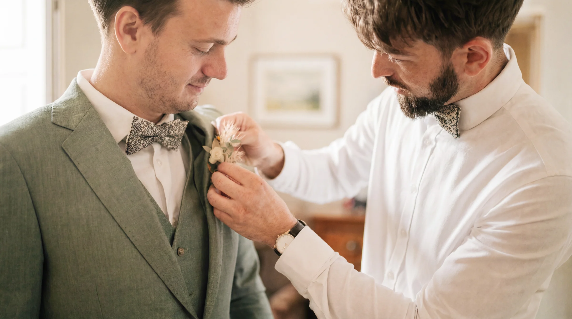 Un homme ajuste la boutonnière florale du marié en costume vert lors d'un reportage mariage à Bourg-lès-Valence, lumière douce
