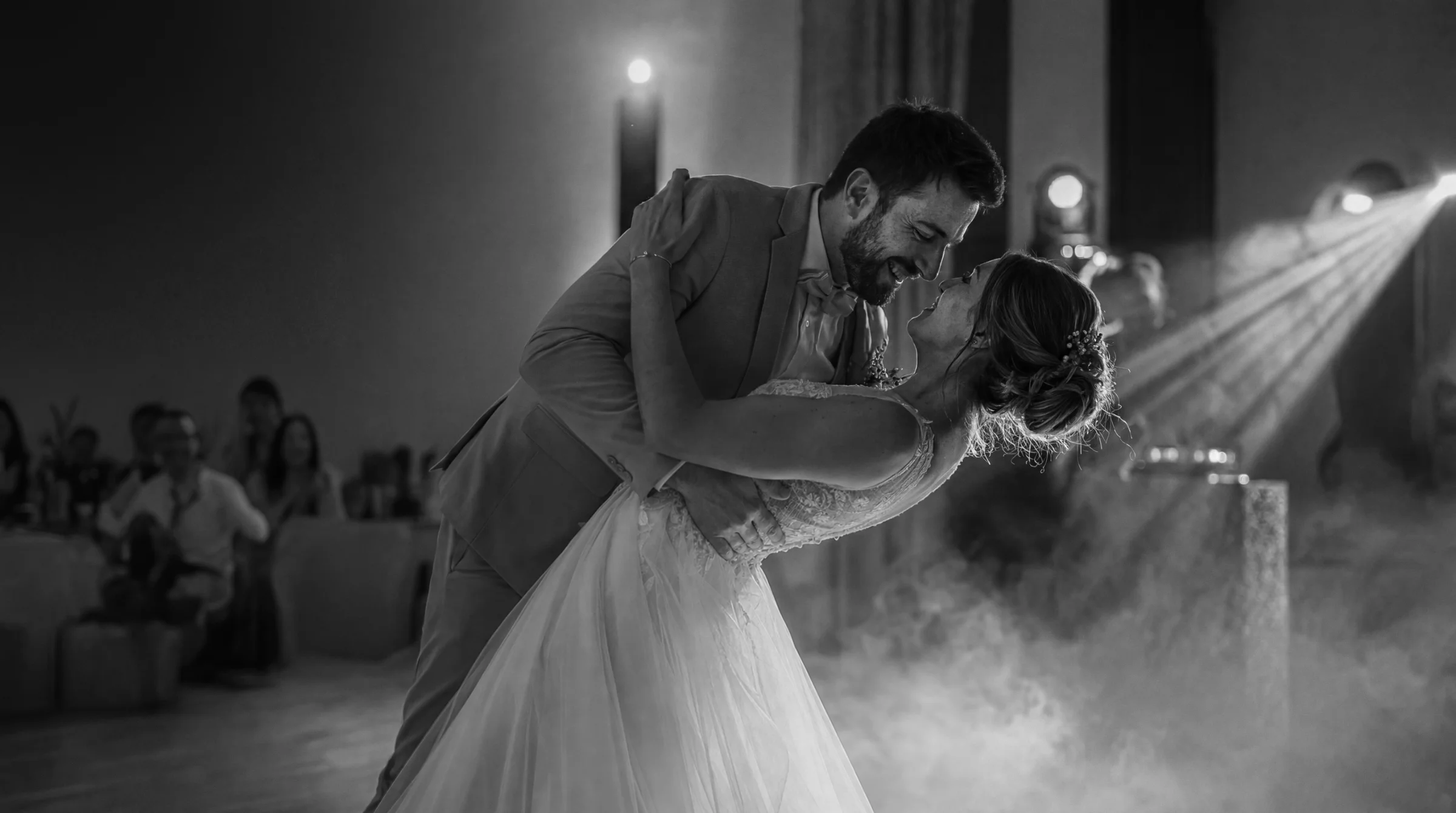 Jeunes mariés dansant un slow romantique à Romans, sous une lumière tamisée et des projecteurs, pour un reportage de mariage