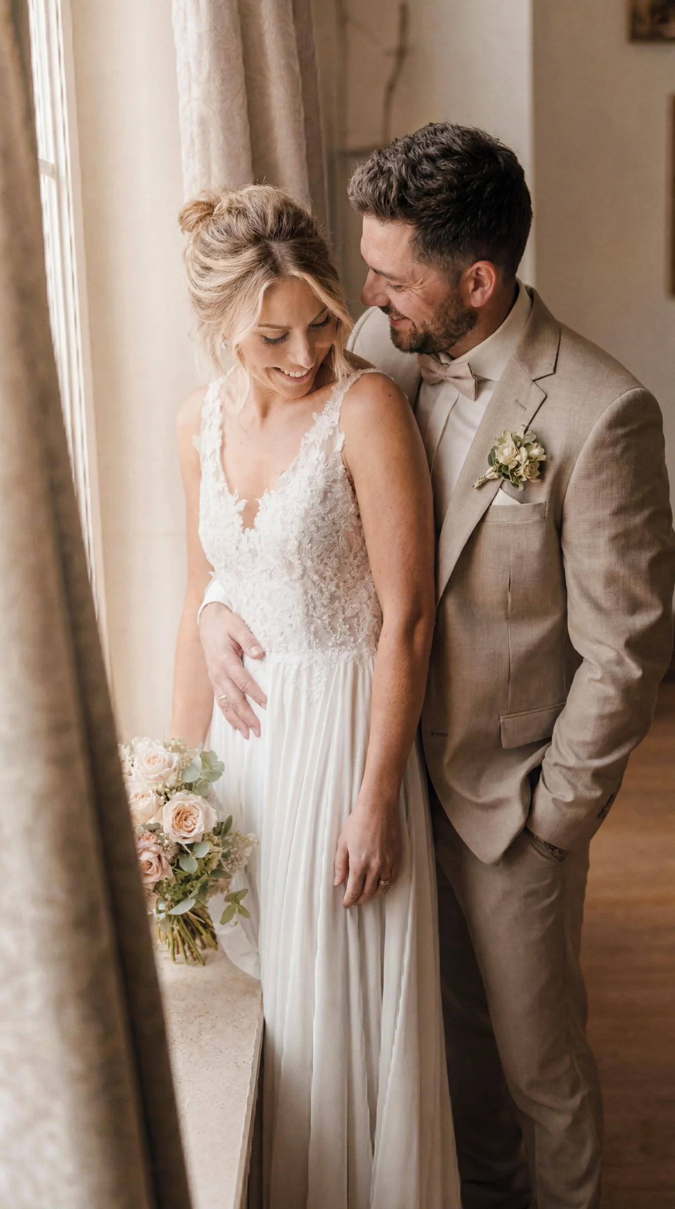 Reportage mariage à Valence, les jeunes mariés souriants et tendres près d'une fenêtre, lumière naturelle douce