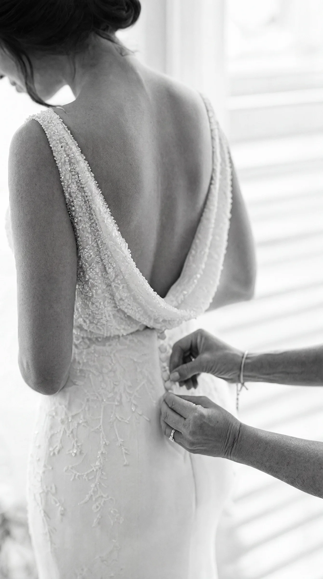 Mains d'une proche aidant la mariée à Romans à boutonner sa robe de mariée perlée, un moment intime du reportage